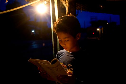 A boy trying to read under dim lighting 